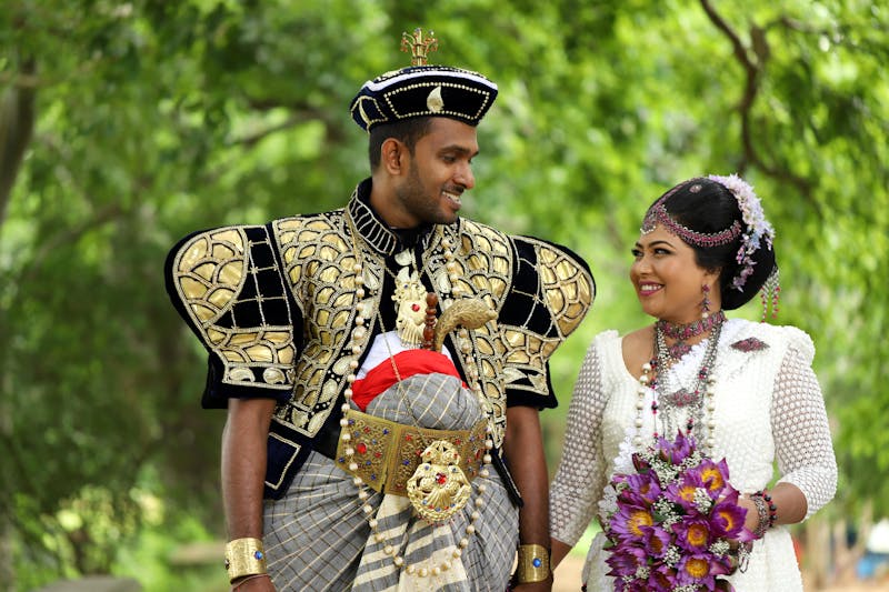 Sri Lankan couple in traditional wedding attire amidst lush green backdrop